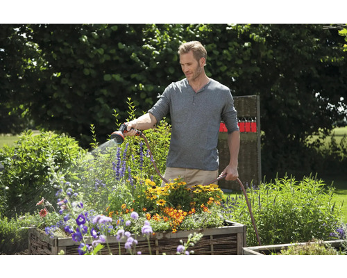 Ein Mann bewässert Blumen mit einem Gartenschlauch im Garten.