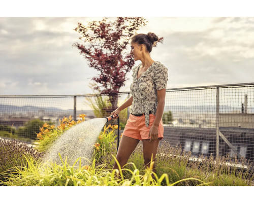 Femme arrosant des plantes sur un toit-terrasse avec un tuyau d''arrosage