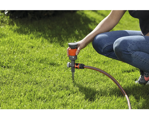 Eine Person stellt einen Rasensprenger auf einem Rasen ein.