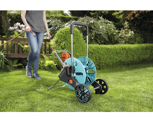 Gartenszene mit einer Person und einem mobilen Schlauchwagen zum Aufrollen eines Gartenschlauchs.