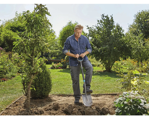 Un homme creuse un trou pour un arbre dans le jardin avec une bêche.