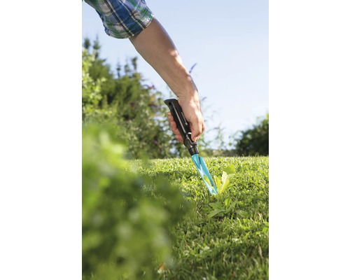 Scène de jardin avec une main utilisant un désherbeur dans la pelouse