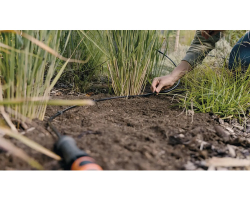 Eine Person verlegt ein Bewässerungssystem im Garten.