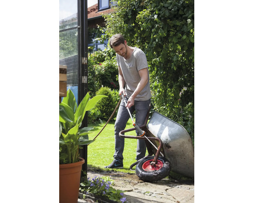 Mann reinigt eine Schubkarre mit einem Gartenschlauch im Garten.