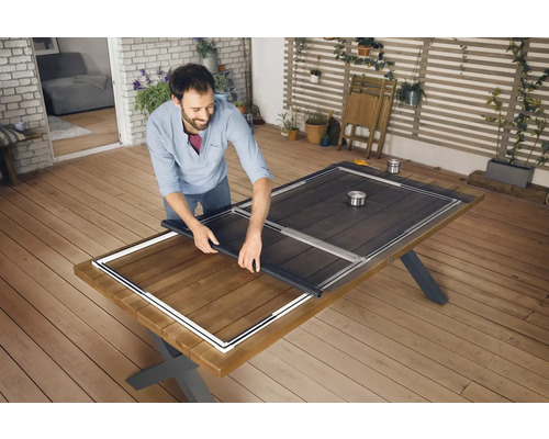 Un homme installe une moustiquaire sur une table en bois à l''extérieur.