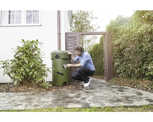 Un homme répare une cuve de récupération d''eau de pluie avec du ruban adhésif dans le jardin.