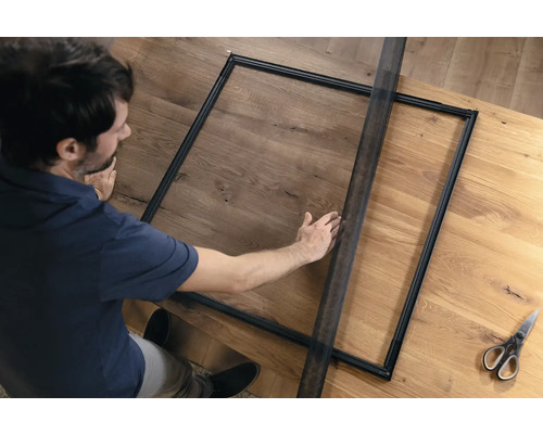 Un homme assemble une moustiquaire sur une table en bois.