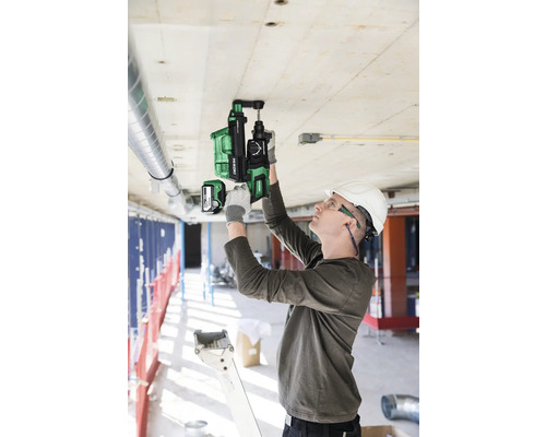 Un homme perce un plafond en béton avec un perforateur sans fil sur un chantier.