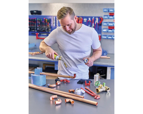 Un homme soude des tuyaux de cuivre avec un brûleur à gaz dans un atelier.