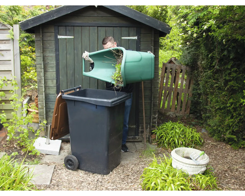 Mann leert Grünabfälle in eine Mülltonne im Garten