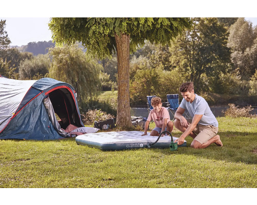Campingplatzszene mit Zelt, Luftmatratze, Vater und Sohn beim Aufpumpen der Matratze mit einer Handpumpe