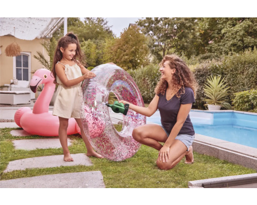 Mutter pumpt Schwimmreifen mit einer Akku-Luftpumpe auf, Tochter steht daneben und ein aufblasbarer Flamingo ist im Hintergrund