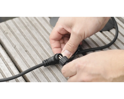 Ein Mann verbindet ein schwarzes Kabel mit einem Stecker auf einer Holzoberfläche.