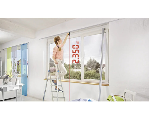 Femme mesurant la hauteur de la pièce avec un télémètre laser sur une échelle