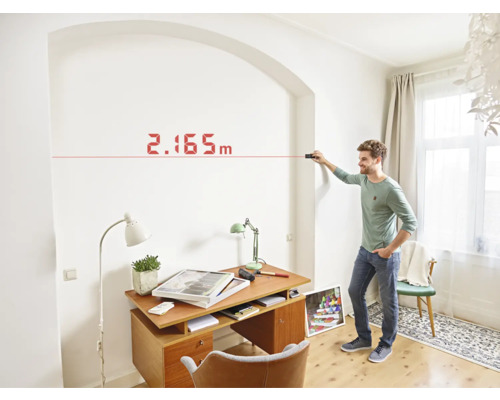 Un homme mesure un mur avec un télémètre laser dans une pièce.