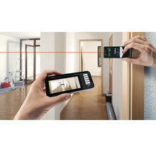 Une personne mesure une pièce avec un télémètre laser et un smartphone. Logo Bosch.
