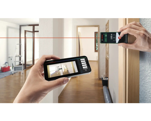 Person misst einen Raum mit einem Laserentfernungsmesser und einem Smartphone. Bosch Logo.