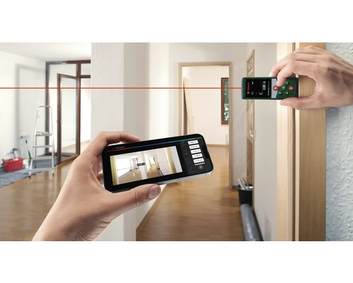 Deux mains tiennent un télémètre et un smartphone dans une pièce pour capturer les dimensions de la pièce à l''aide de la technologie laser.