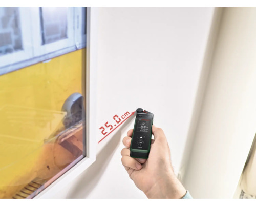 Une personne mesure la distance sur un mur avec un télémètre laser.