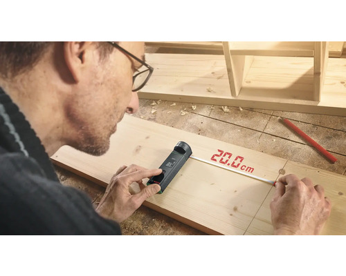 Artisan mesurant une planche de bois avec un télémètre numérique.