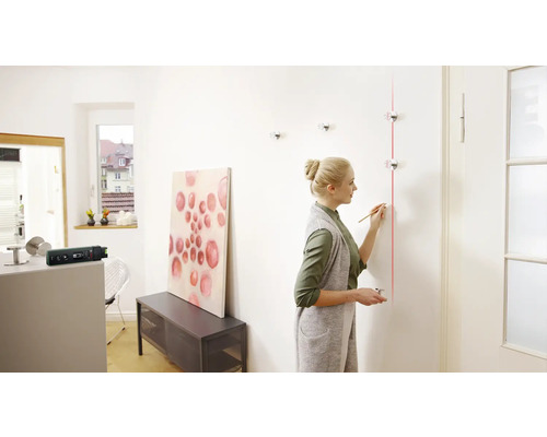 Une femme aligne un porte-manteau sur un mur avec un laser à lignes