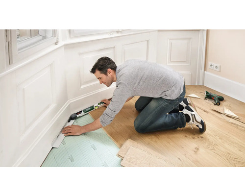 Ein Mann verlegt Laminatboden mit einer Wasserwaage im Zimmer.