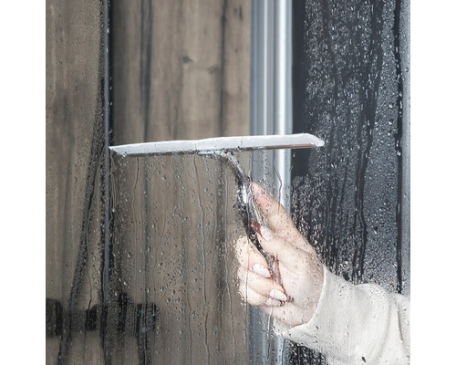 Une personne utilise une raclette de douche pour nettoyer une paroi de douche.