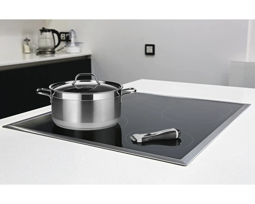 Edelstahltopf mit Deckel auf einem Induktionskochfeld mit Reinigungsschaber in einer hellen Küche.