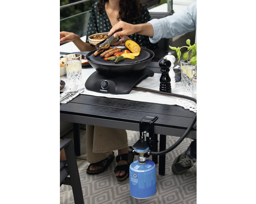 Personen grillen Würstchen und Gemüse auf einem Tischgrill mit Gaskartusche.