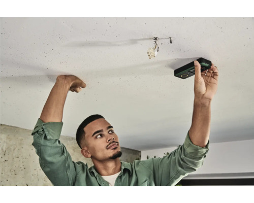 Un homme utilise un appareil de mesure numérique sur un plafond.