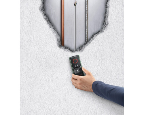 Une main tient un détecteur devant un mur avec des câbles apparents