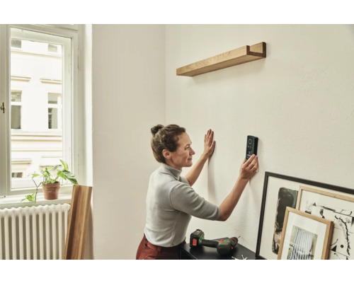 Une femme utilise un télémètre laser pour fixer une étagère en bois au mur.