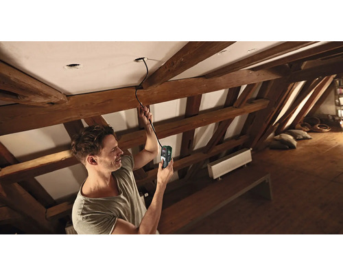 Ein Mann benutzt ein Messgerät zur Kabelsuche an einer Decke in einem Dachgeschoss.