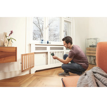 Ein Mann verwendet ein Thermometer zur Messung der Temperatur eines Heizkörpers in einem hellen Raum.