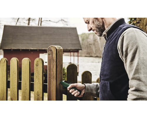 Ein Mann verwendet ein Holzfeuchtemessgerät an einem Holzzaun.