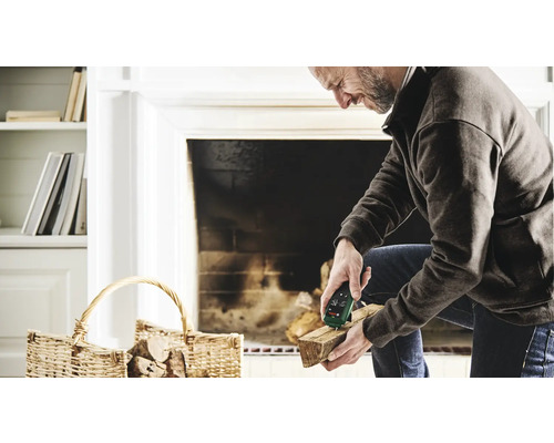 Ein Mann misst die Holzfeuchtigkeit mit einem Messgerät vor einem Kamin.