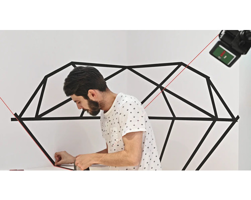 Un homme colle un motif géométrique au mur avec du ruban adhésif