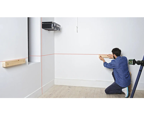 Un homme fixe une construction en bois à un mur à l''aide d''un laser et de lattes de bois.