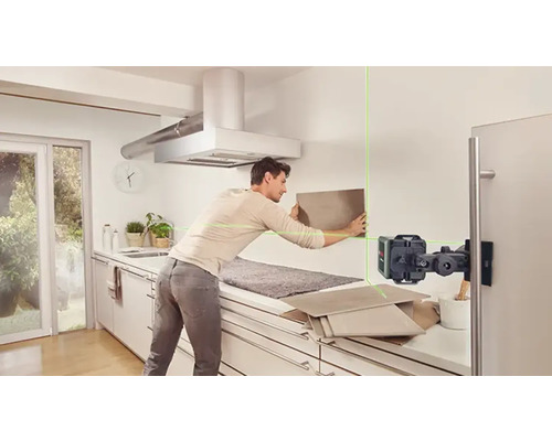 Un homme fixe des carreaux avec un laser linéaire dans une cuisine