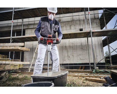 Un ouvrier du bâtiment mélange du mortier dans une cuve avec un mélangeur électrique de mortier sur un chantier.