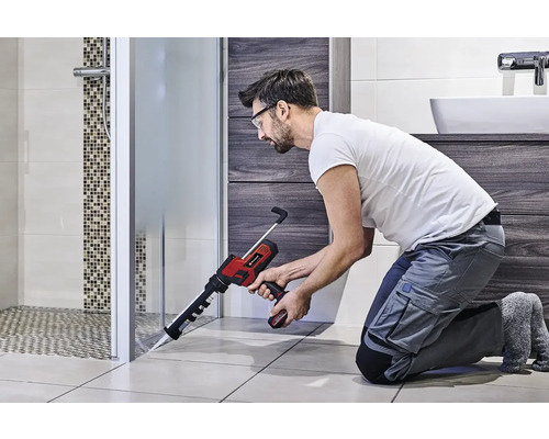 Un artisan utilise un pistolet à cartouche sans fil dans la salle de bain pour sceller une cabine de douche.