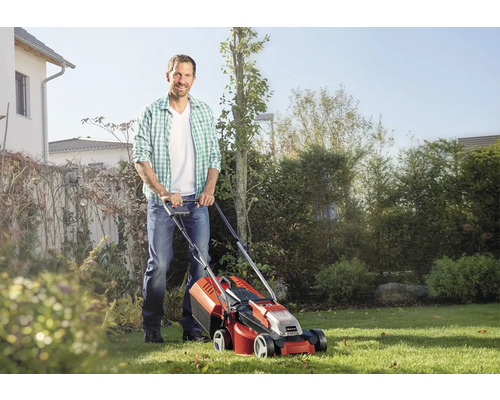 Un homme tond le gazon avec une tondeuse à gazon à batterie dans le jardin.