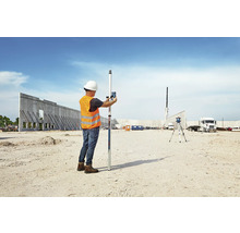 Un homme portant un casque de chantier et un gilet de sécurité utilise un niveau sur un chantier de construction.