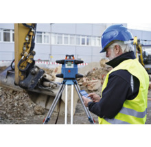 Ouvrier du bâtiment avec laser rotatif sur le chantier avec une excavatrice en arrière-plan