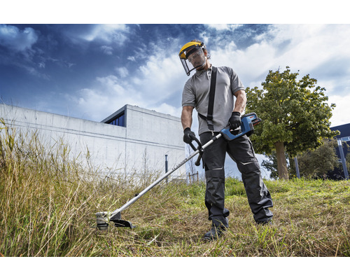 Eine Person benutzt einen Rasentrimmer mit Schutzvisier im Garten.