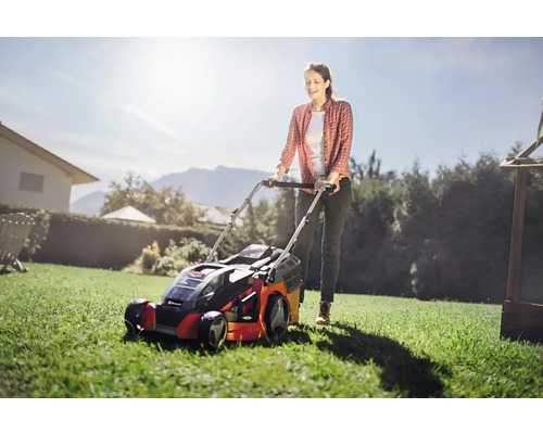 Frau mäht Rasen mit einem Rasenmäher im Garten.