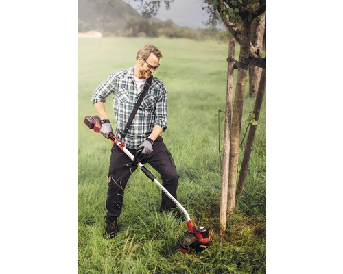 Ein Mann trimmt Gras mit einem Akku-Rasentrimmer in einem Garten.