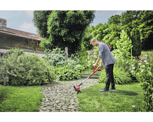 Mann verwendet einen Akku-Rasentrimmer im Garten.