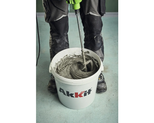 Un artisan mélange de la colle à carrelage dans un seau de la marque Akkit avec un mélangeur électrique.