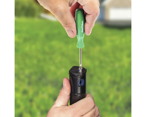 Eine Person justiert einen Regner mit einem Schraubendreher von Rain Bird.